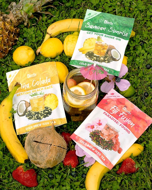 Assorted custom printed pouches for tea, coconut, and snack products arranged outdoors among fruit and greenery